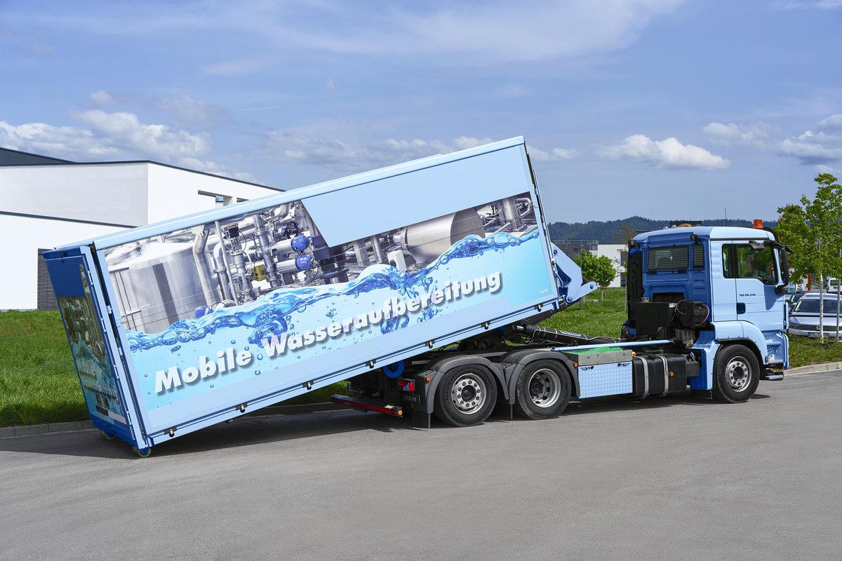 Ein blauer Lastwagen mit einem Container für mobile Wasseraufbereitung, der auf einer Straße steht.