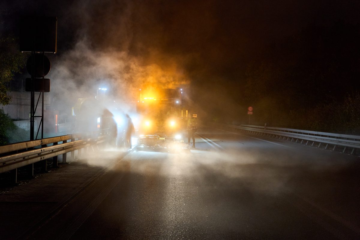 Ein Lastwagen mit gelben Lichtern und zwei Personen auf einer nebligen Straße bei Nacht.