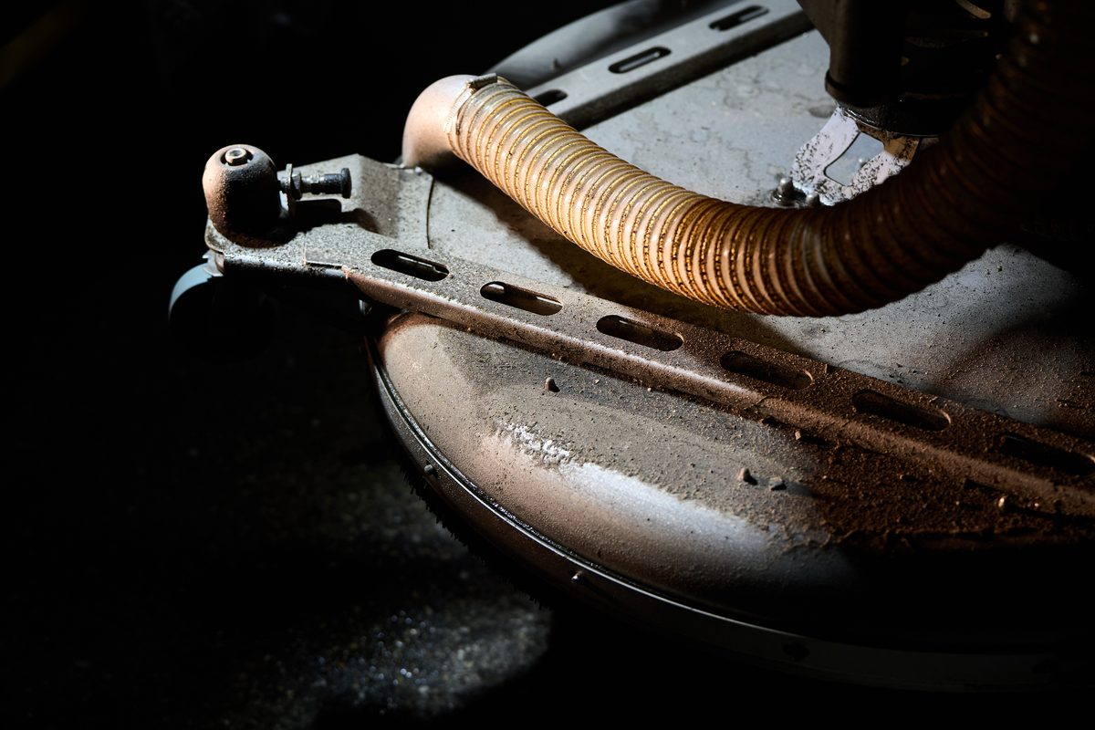 Nahaufnahme eines staubigen, grauen Industriegeräts mit einem gerippten Schlauch und Metallstreben.