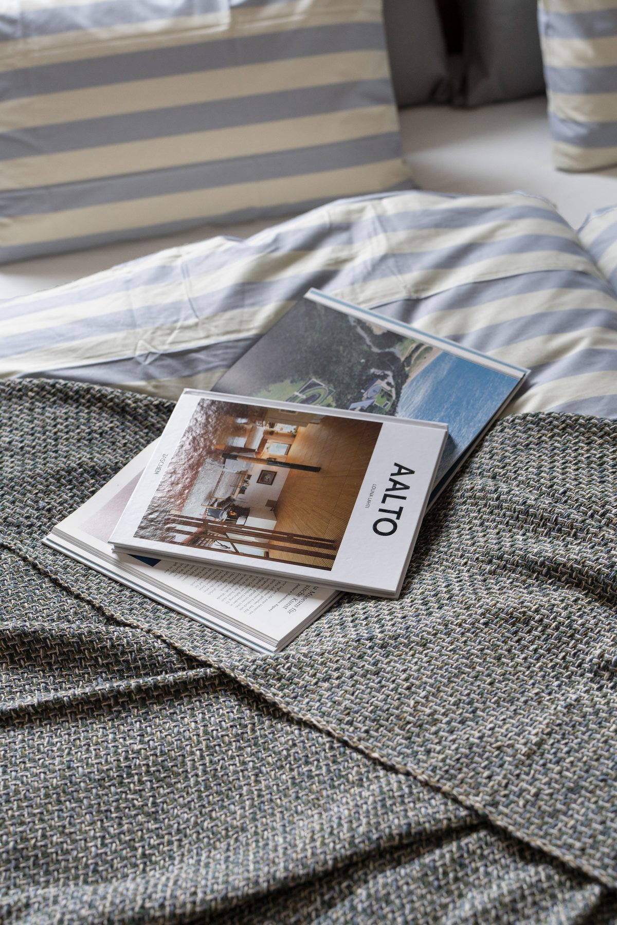 Zwei Bücher liegen auf einer grauen Decke mit gestreifter Bettwäsche im Hintergrund.