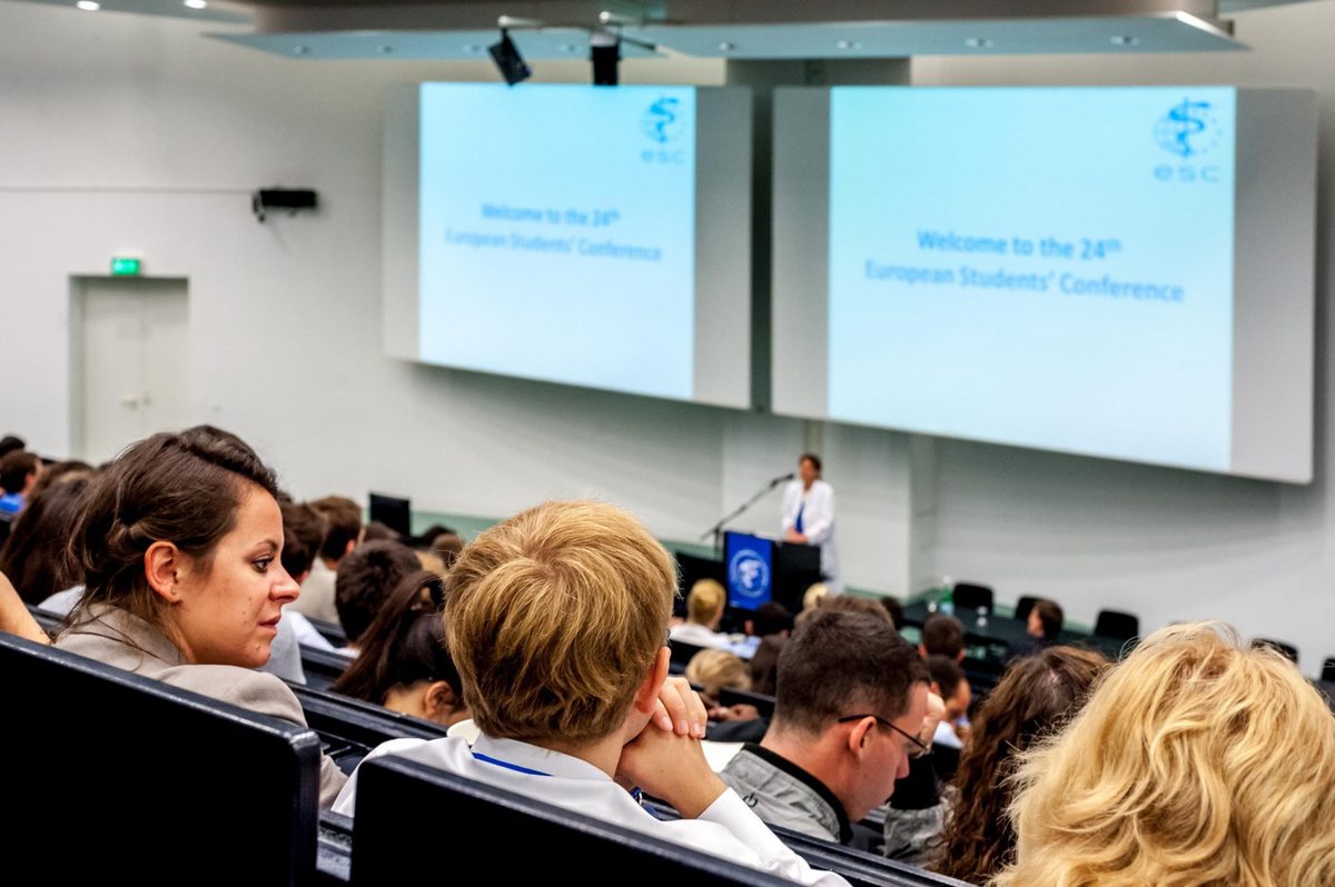 Zuhörer in einem Hörsaal blicken auf eine Rednerin und zwei Leinwände mit der Aufschrift 'Welcome to the 24th European Students'