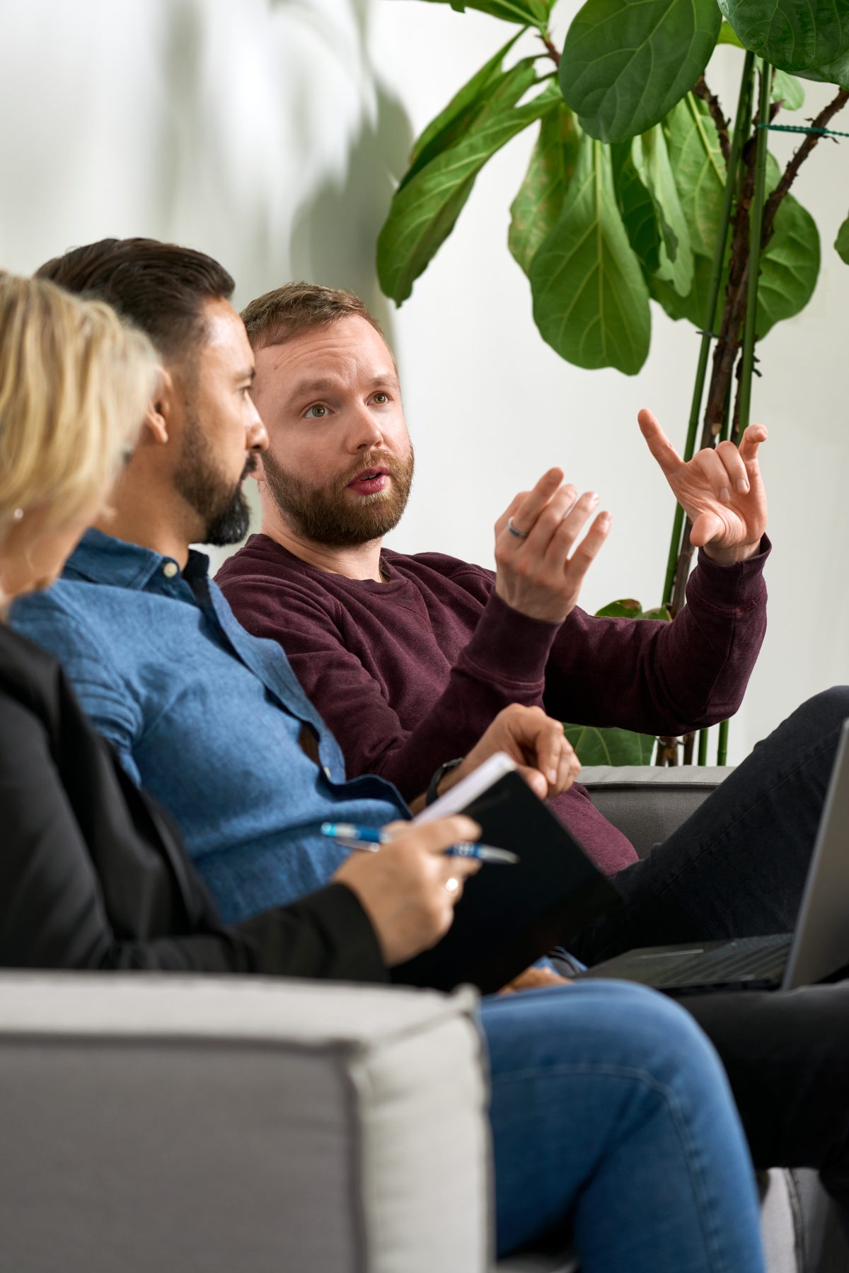 Drei Personen sitzen auf einem Sofa, der Mann in der Mitte gestikuliert mit den Händen, während er spricht.
