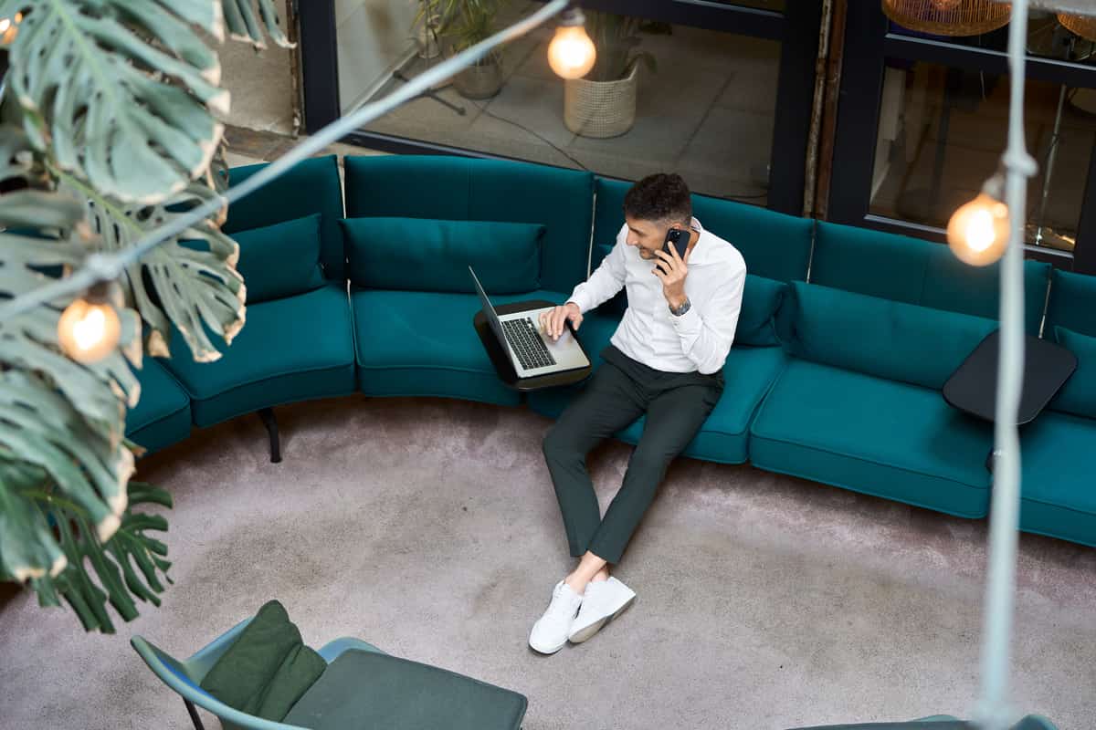 Vogelperspektive: Giuseppe Conforti auf türkisem Sofa mit Laptop und Telefon, Lokhalle Freiburg.