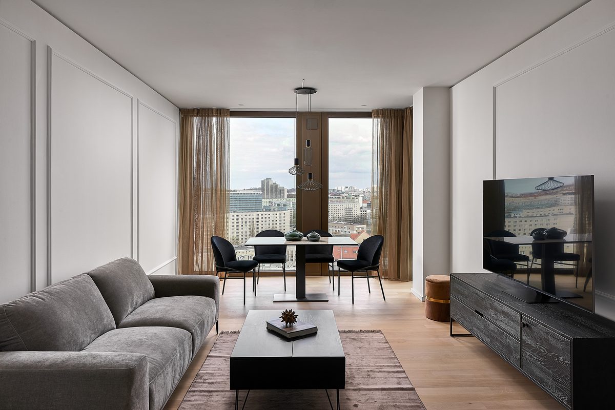 Ein modernes Wohnzimmer mit grauem Sofa, Couchtisch, Esstisch mit vier Stühlen und einem Fernseher auf einem Sideboard.