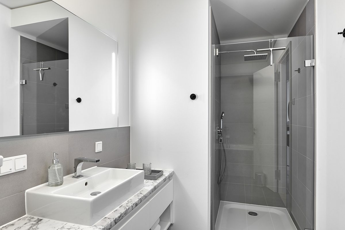 Modernes Badezimmer mit weissem Waschbecken auf Marmorplatte, beleuchtetem Spiegel und Duschkabine mit Glaswand.