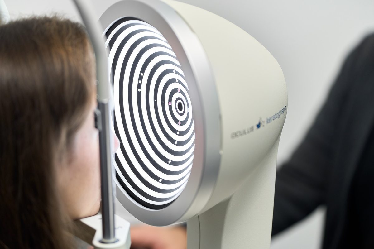 Eine Person blickt in ein ophthalmologisches Gerät mit einem beleuchteten Muster aus schwarzen und weißen Kreisen.