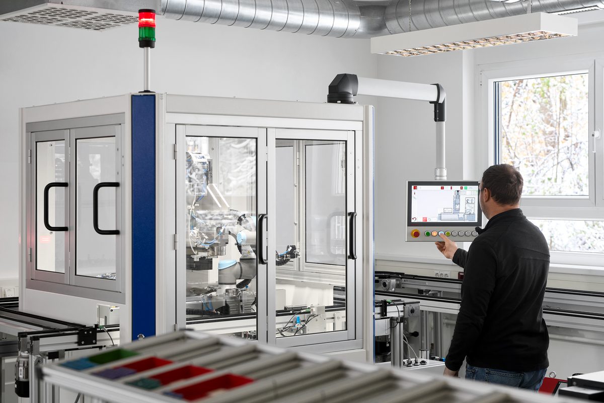 Ein Mann bedient ein Touchscreen-Display neben einer Maschine mit Glasfront und einem Roboterarm.