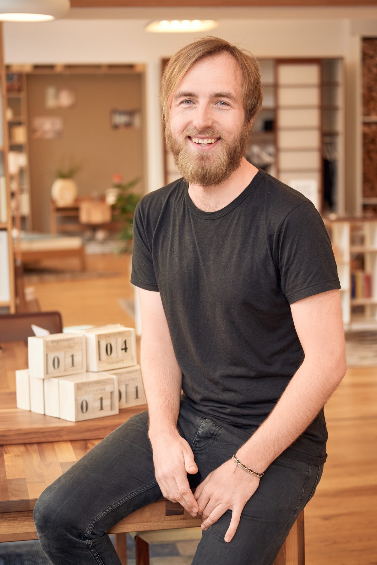 Holzconnection: Ein lächelnder Mann mit Bart und blonden Haaren sitzt auf einem Holztisch neben einem Holzkalender