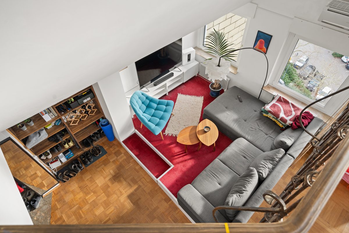 Blick von oben auf ein Wohnzimmer mit rotem Teppich, grauem Sofa, blauem Sessel und einem Schuhregal.
