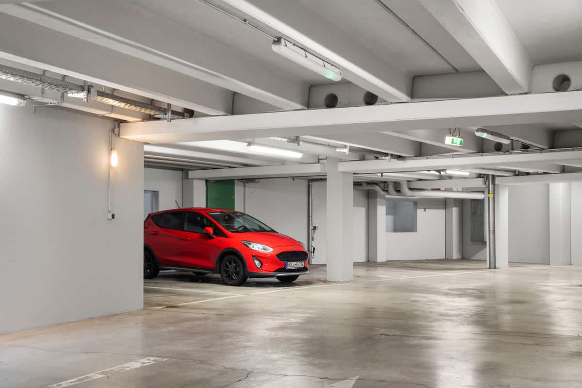 Innenansicht der Tiefgarage mit einem roten Auto auf einem Stellplatz, Betondecke und Stützen im Hintergrund.