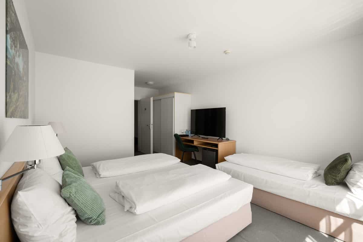 Zimmer mit zwei Betten, einem Landschaftsbild über dem Kopfende, Schreibtisch mit Fernseher und Einbauschrank.