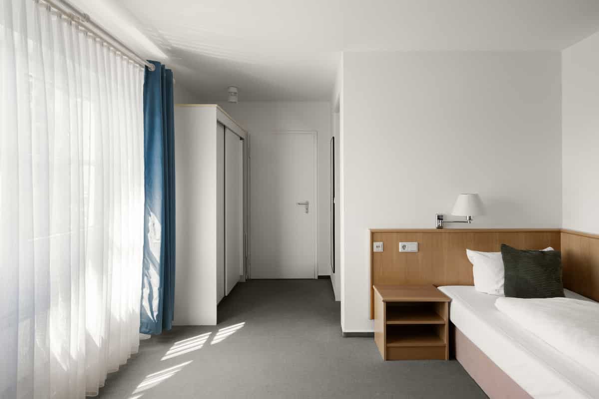 Zimmerflur mit Einbauschrank, Blick zur Badezimmertür und petrolfarbenem Vorhang am Fenster.