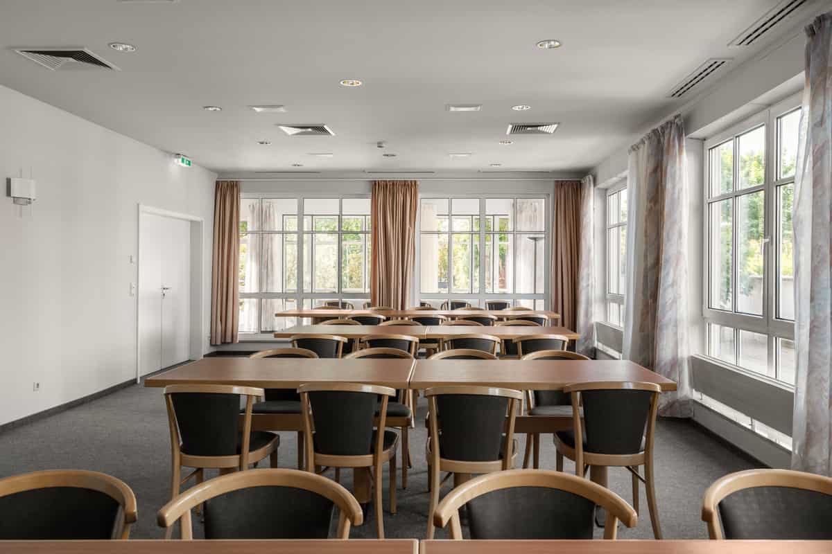 Tagungsraum mit Tischreihen im Klassenzimmer-Stil, Stühlen und großen Fenstern.