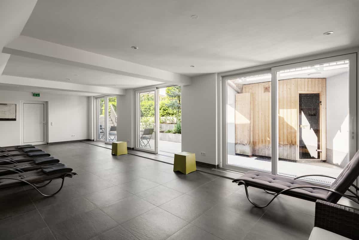 Ruheraum des Wellness-Bereichs mit Relaxliegen und Blick durch große Glastüren auf die Außensauna aus Holz.
