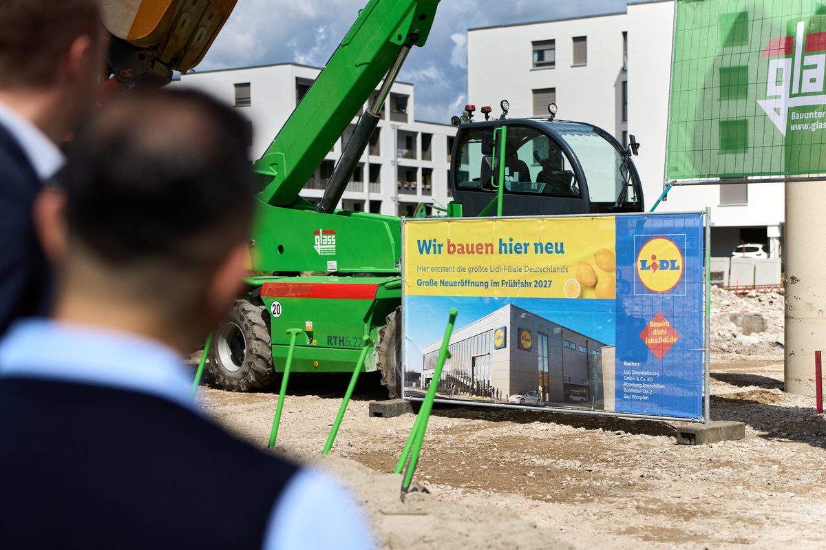 Lidl-Bautafel &bdquo;Wir bauen hier neu&ldquo; mit Baugerät auf dem Baufeld