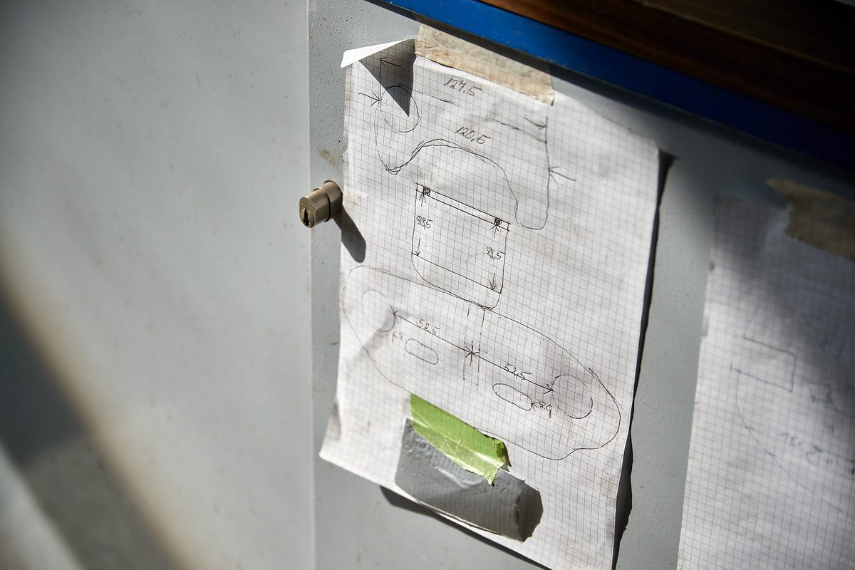 Ein kariertes Blatt Papier mit einer Skizze und Maßen ist mit Klebeband an einer hellgrauen Wand befestigt.