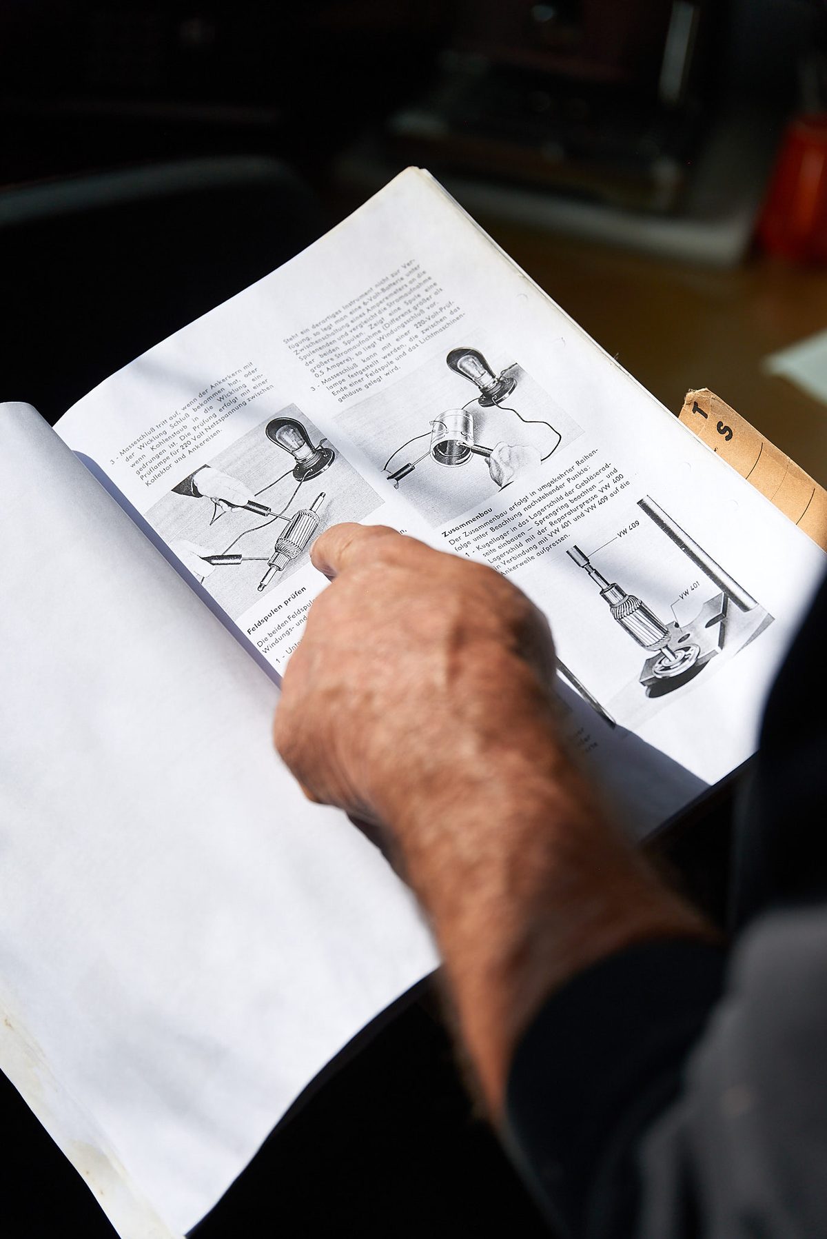 Eine Hand zeigt auf eine technische Zeichnung in einem geöffneten Handbuch.