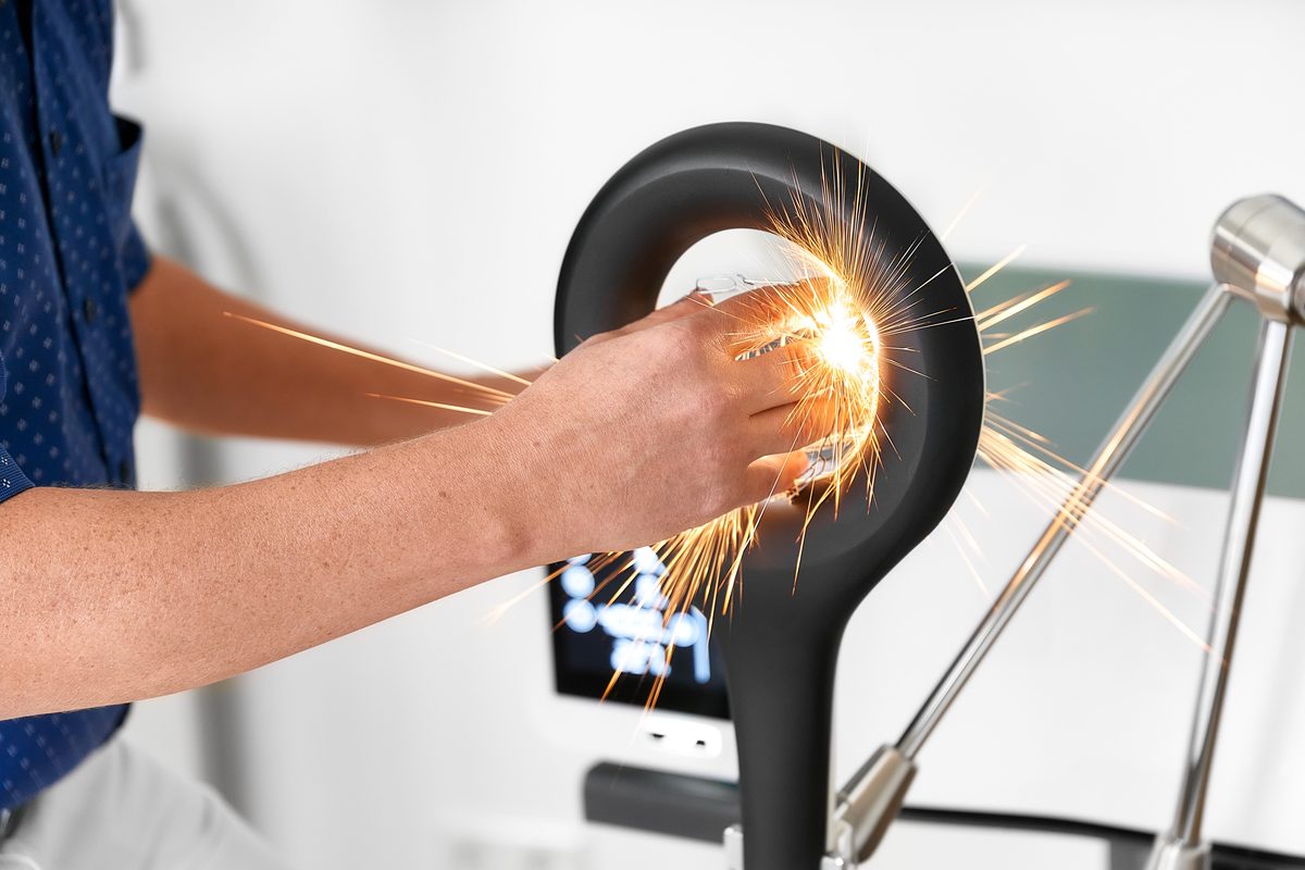 Eine Person hält ein Metallstück an eine Schleifmaschine, Funken sprühen.