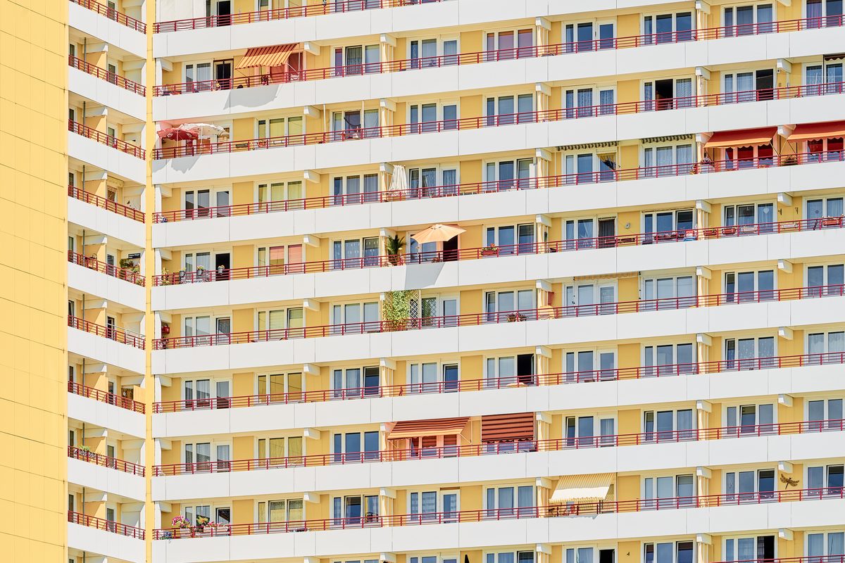 Fassade eines gelben Hochhauses mit vielen Balkonen, roten Geländern und Markisen in Berlin-Marzahn.