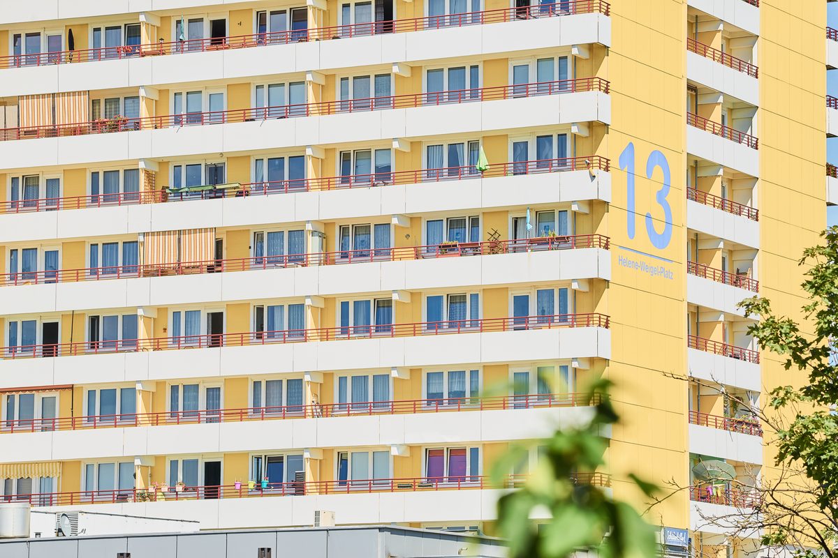 Fassade eines gelben Hochhauses mit vielen Balkonen und Fenstern, die Hausnummer 13 ist groß aufgemalt.