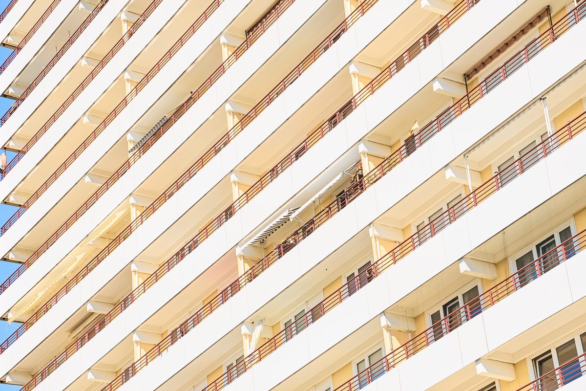 Fassade eines Hochhauses mit vielen Balkonen, die durch rote Gitter und weiße Brüstungen begrenzt sind.