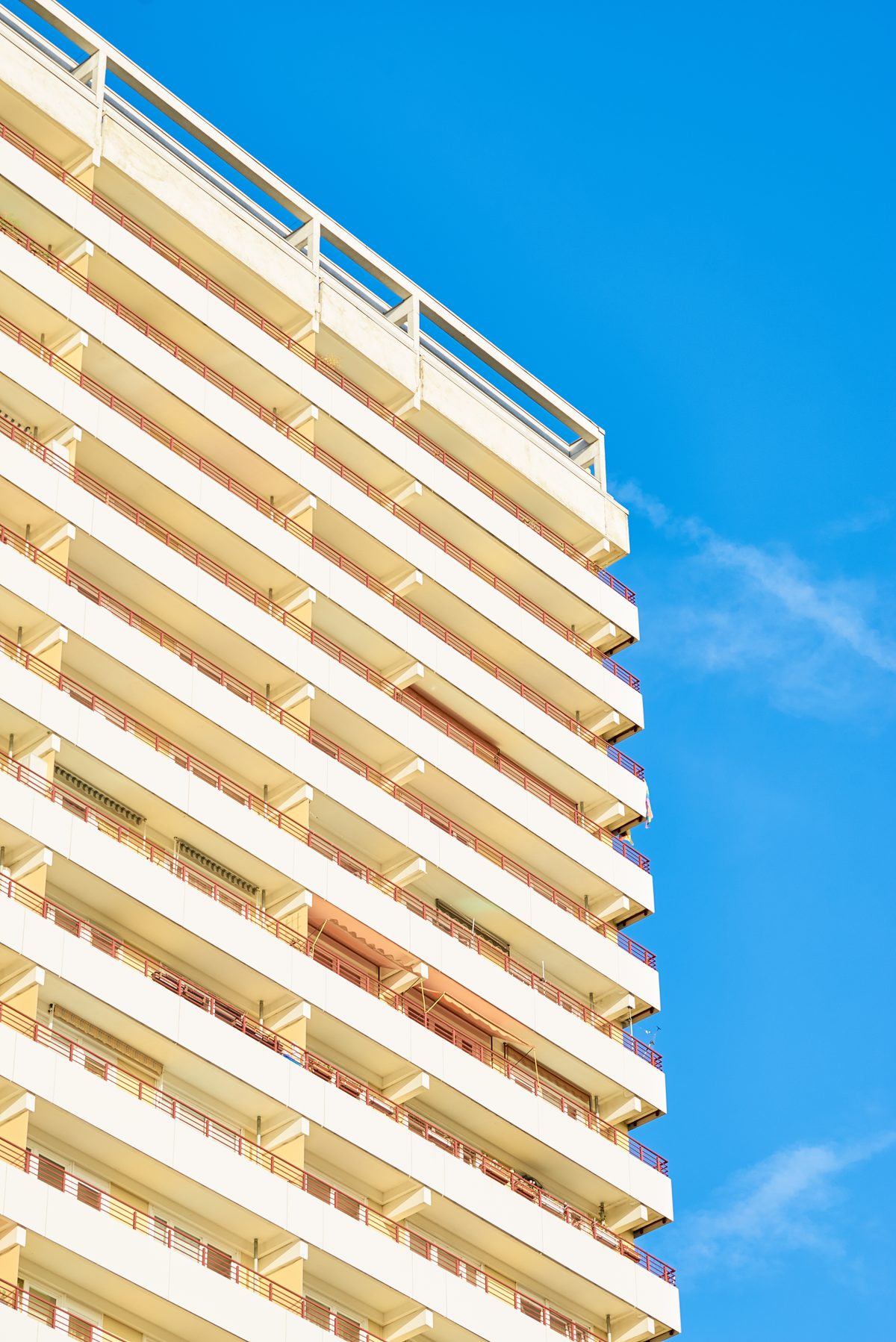 Fassade eines Hochhauses mit vielen Balkonen und roten Geländern unter blauem Himmel.