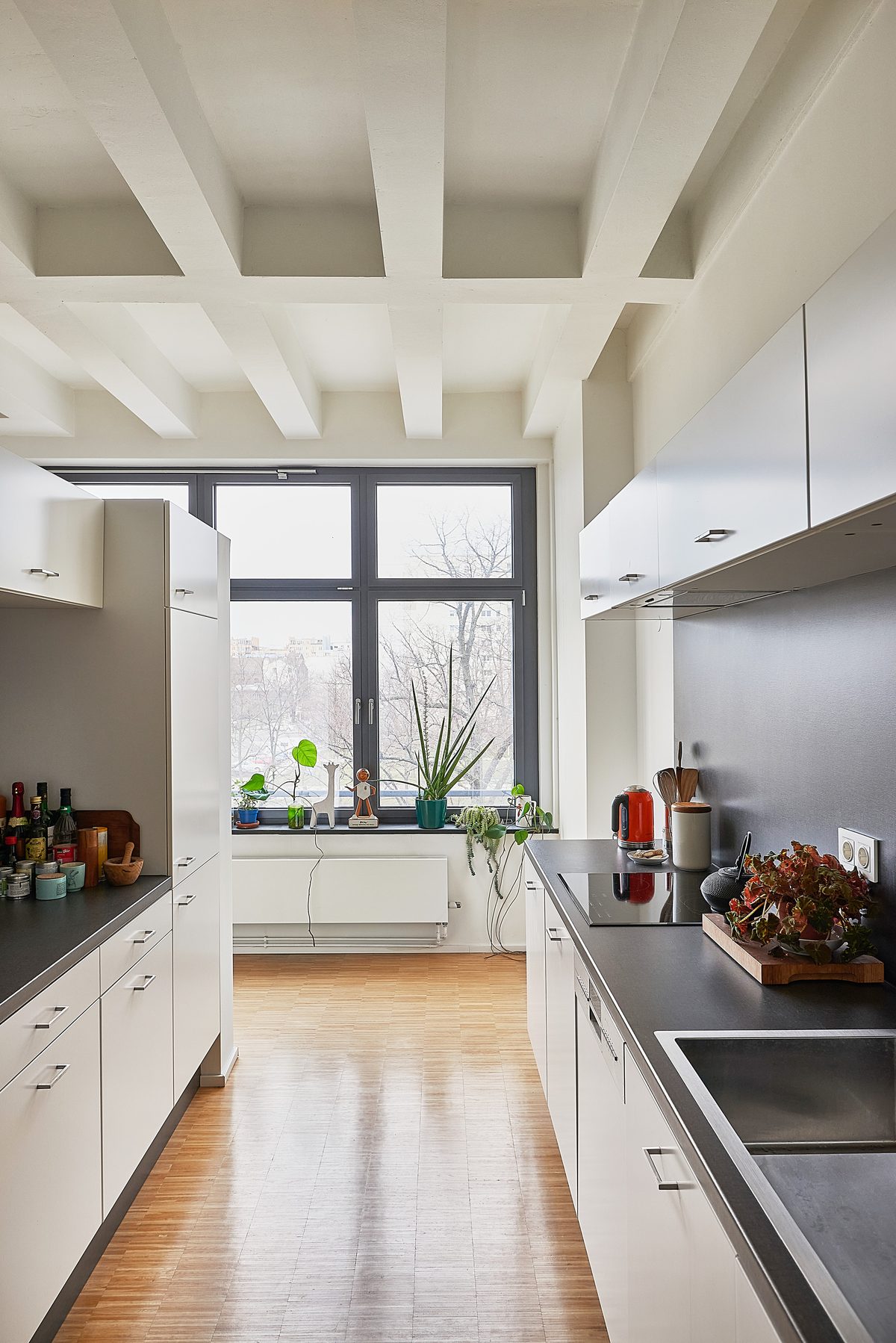Eine moderne Küche mit weißen Schränken, dunklen Arbeitsplatten, Holzboden und einem großen Fenster mit Pflanzen.