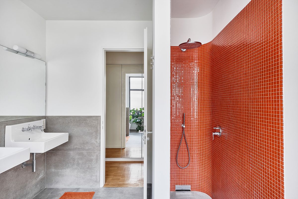 Ein Badezimmer mit zwei Waschbecken, einer Duschkabine mit orangefarbenen Fliesen und einem offenen Durchgang zu einem anderen Raum.